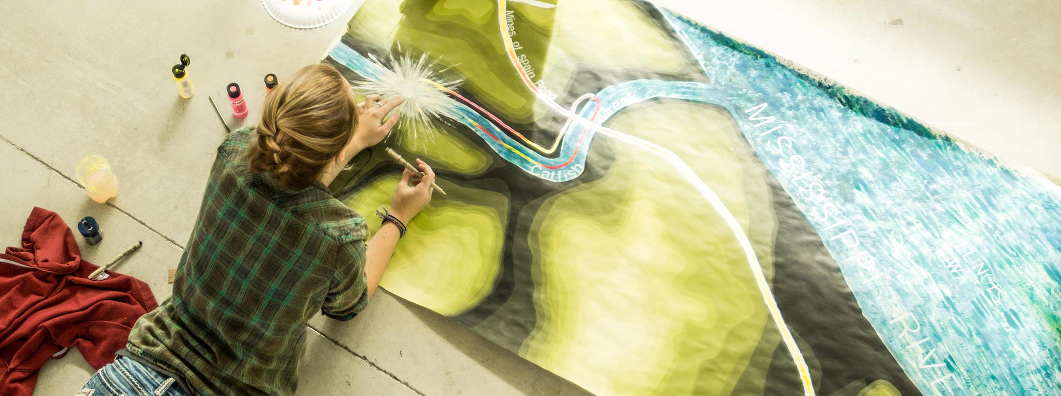 A student paints project on the floor.