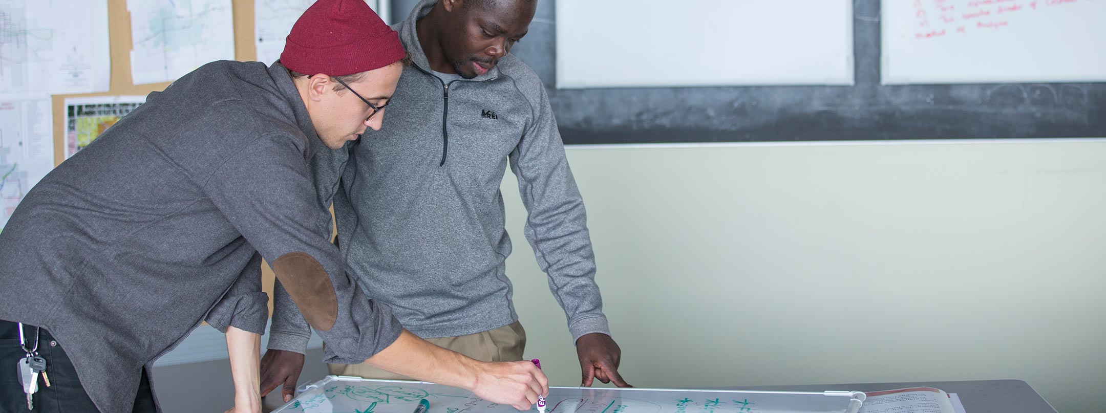 Two design students working on a project and communicating their design on a whiteboard.