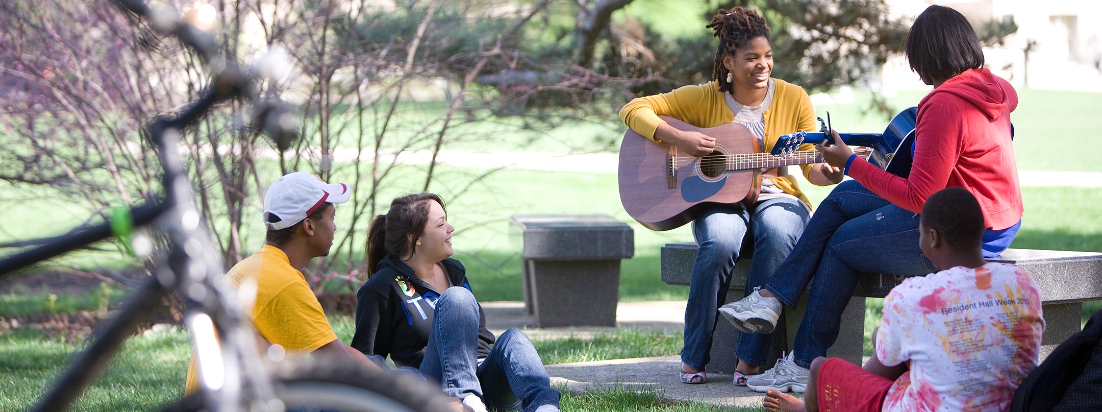 A student plays the guitar outside while peers listen.